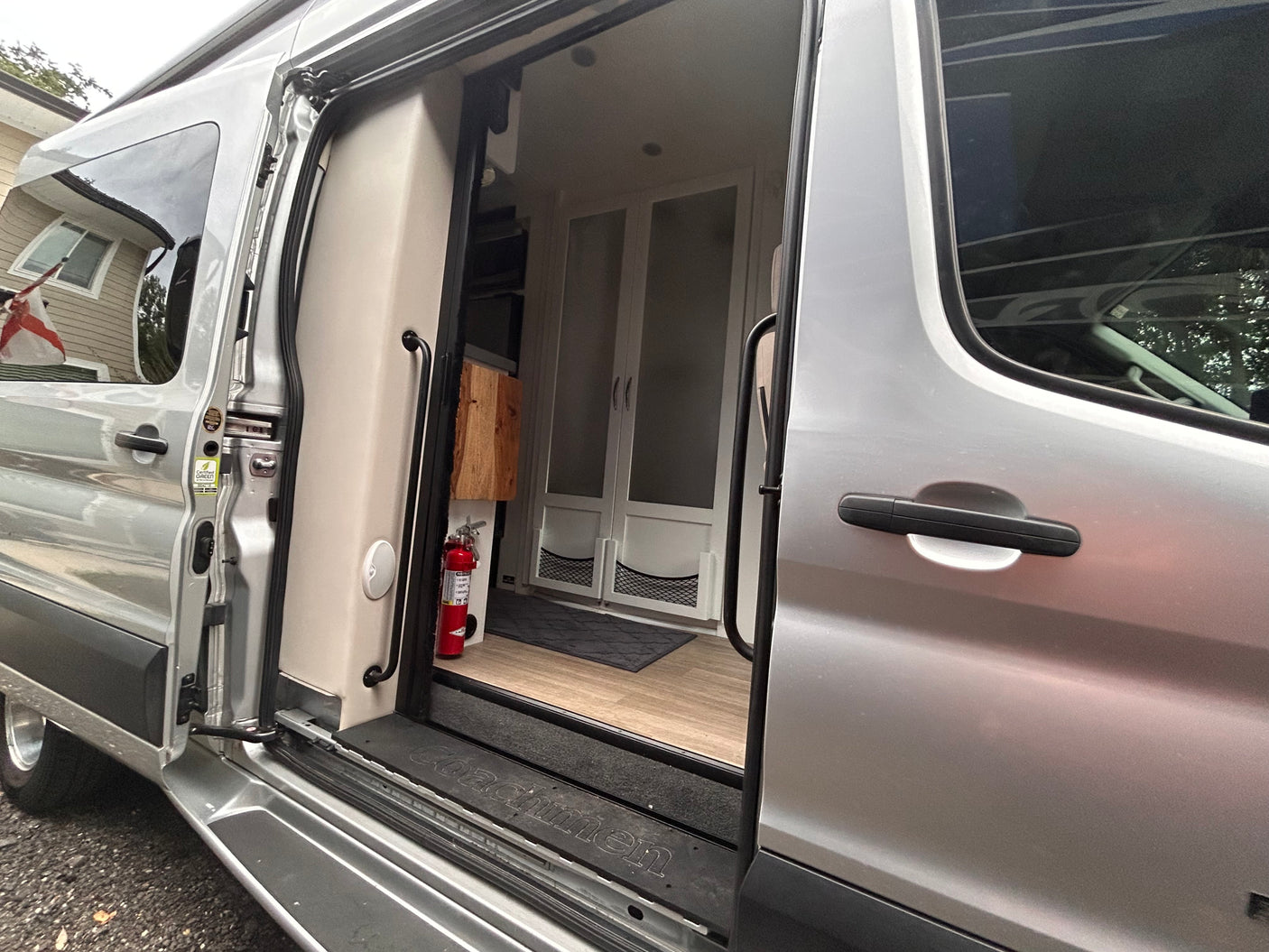 Silver RV rental with open side door revealing clean campervan interior, wood floor, cabinets & fire extinguisher.