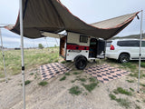 An rv rental teardrop trailer with an awning provides shade for outdoor camping next to a white SUV.