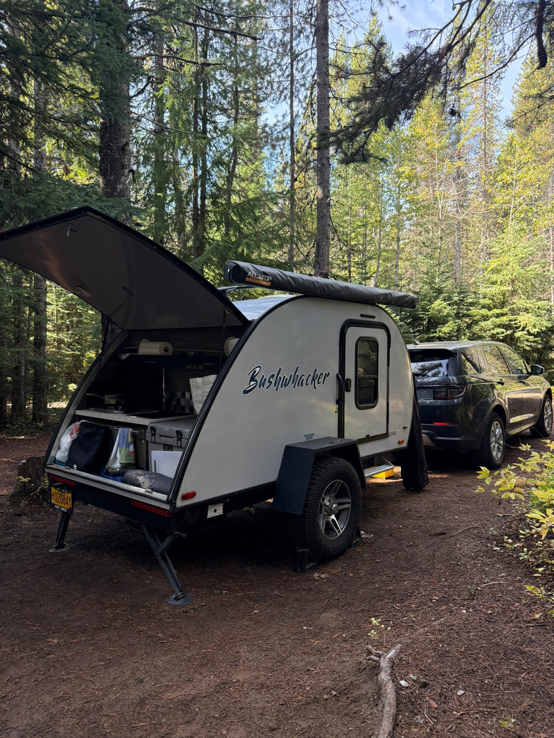 RV rental adventure: Bushwhacker teardrop camper & SUV amidst tall forest trees, kitchen open for camping. — photo 1