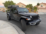 Black Jeep Gladiator truck with a hard-shell roof-top tent, parked curbside. A versatile rv rental alternative!