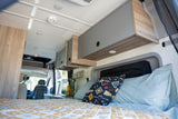 Step inside this cozy RV rental's interior, featuring a comfortable bed, overhead cabinets, and a compact kitchen.