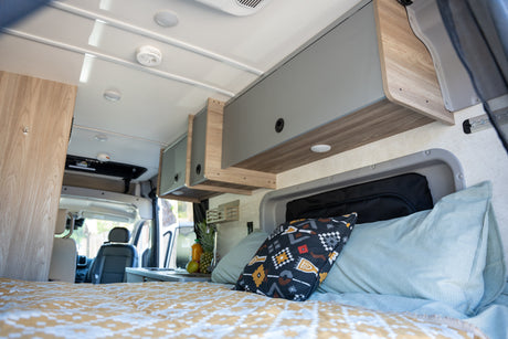 Step inside this cozy RV rental's interior, featuring a comfortable bed, overhead cabinets, and a compact kitchen.
