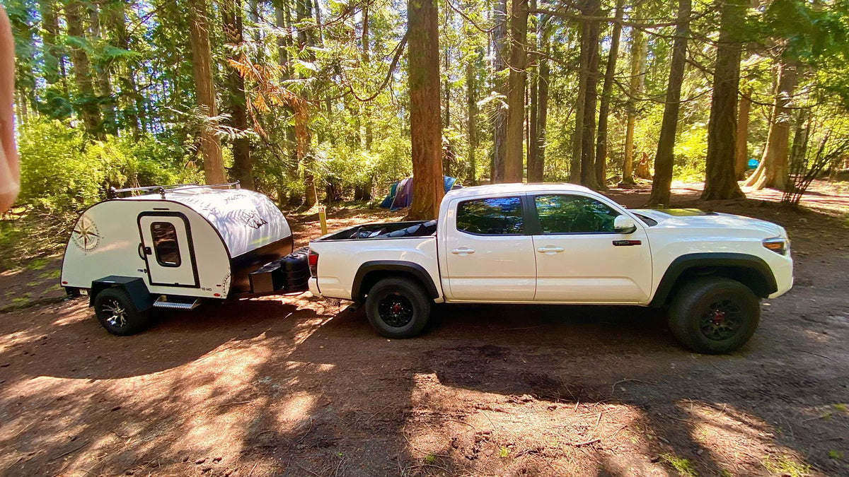 White Toyota Tacoma truck towing a teardrop camper at a sunny forest campsite. Find your ideal RV rental adventure here. — photo 20