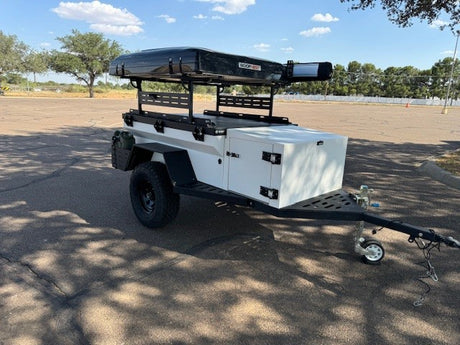 White off-road expedition trailer with roof-top tent & storage, ideal for RV rental. Parked on asphalt lot.