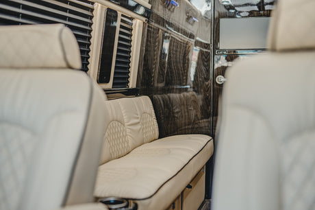 Premium RV rental interior: elegant cream upholstered seating, glossy wood walls, and privacy blinds.