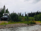 Overcast day camping in an RV rental truck camper by a tranquil forest river.