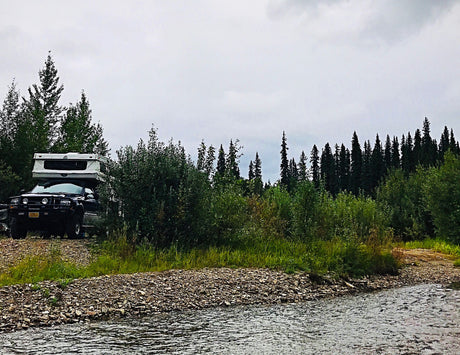 Overcast day camping in an RV rental truck camper by a tranquil forest river.