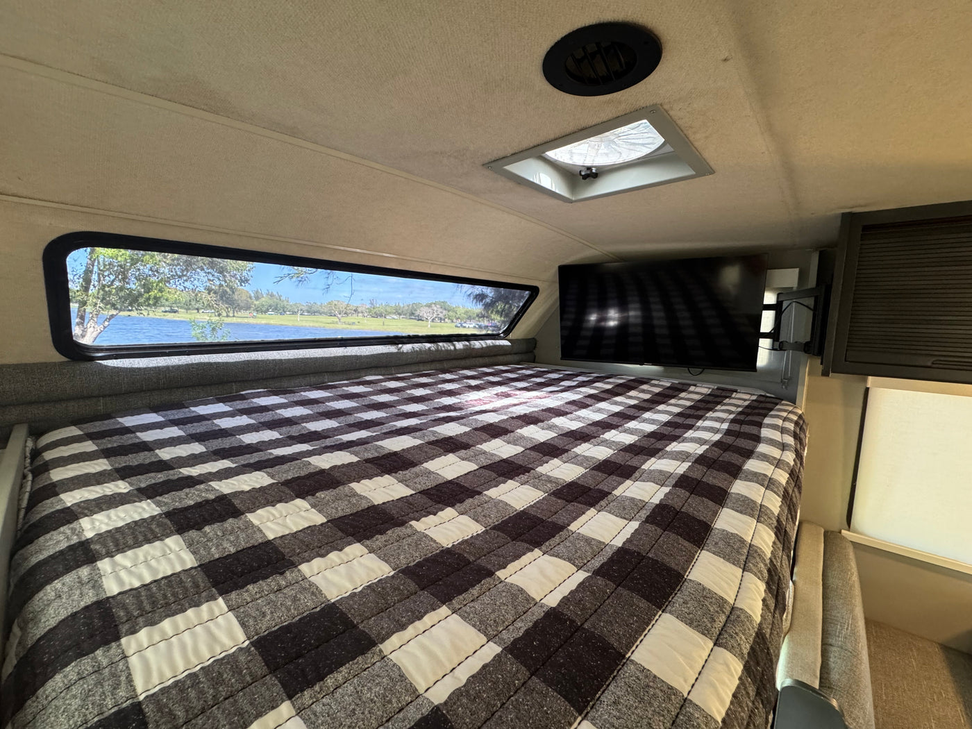 RV rental bedroom: plaid bed, lake view from window, TV, and ceiling vent. Cozy and scenic interior for your trip. — photo 7