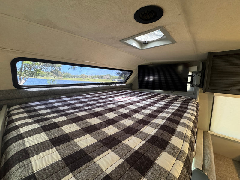 RV rental bedroom: plaid bed, lake view from window, TV, and ceiling vent. Cozy and scenic interior for your trip. — photo 7