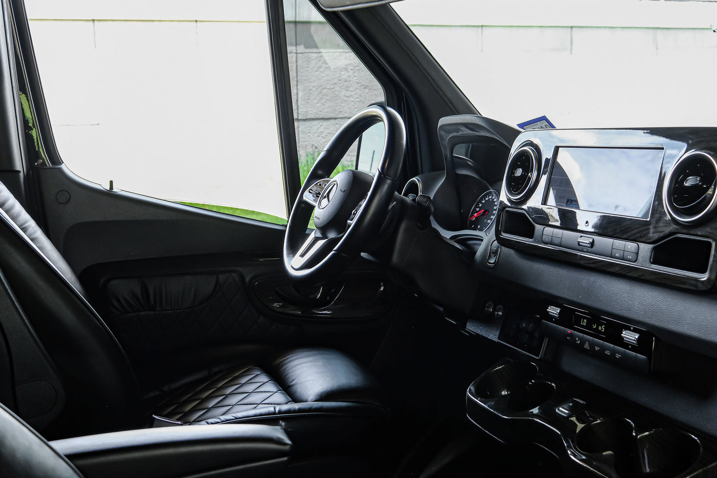 Inside a modern RV rental, showing the driver's area with a detailed dashboard, steering wheel, and quilted black leather seats.