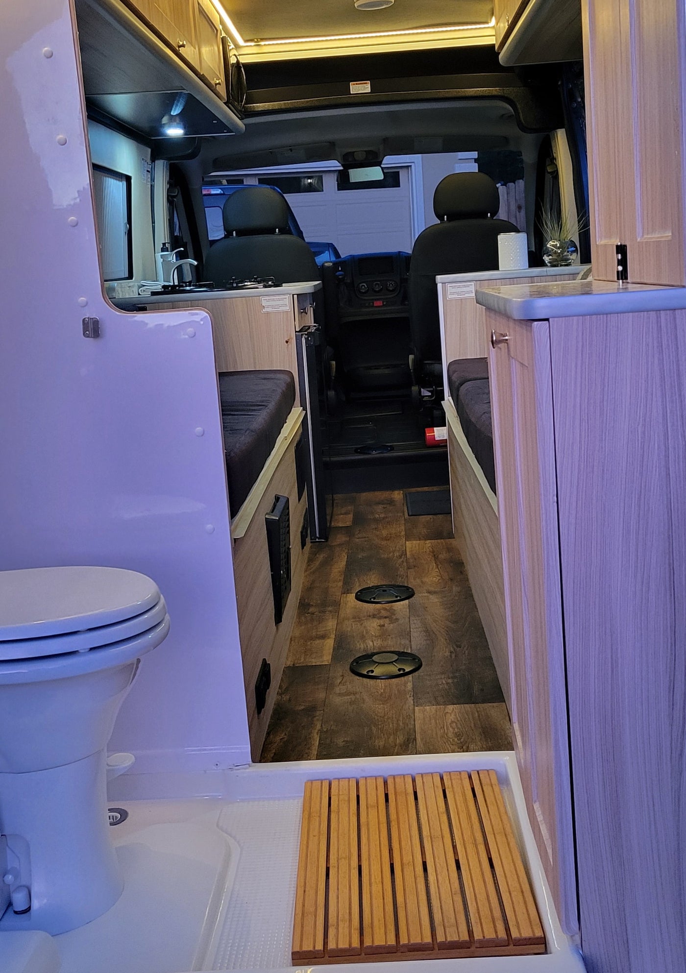 Interior of an RV rental: a fully equipped kitchen, convertible beds, and a compact bathroom with toilet and wooden mat. — photo 10