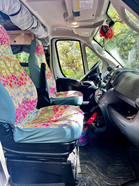 RV rental interior: comfy floral seat covers, overhead storage, and nature views through the front window.