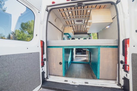 Inside a custom camper van, ideal for rv rental: elevated bed, under-bed storage, wood slat ceiling. Ready for adventure.