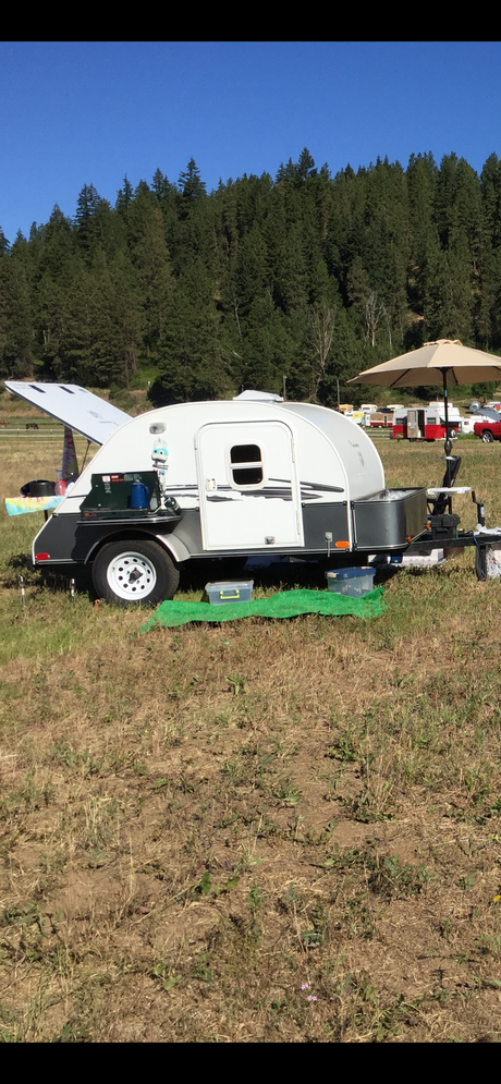 Teardrop RV trailer set up with an open kitchen hatch in a grassy field. Perfect for your next RV rental adventure!