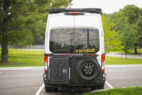 Rear view of a white custom camper van for RV rental, with a spare tire and storage on the back, parked outdoors.