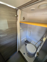 RV rental's compact wet bath featuring a toilet, shower, and practical wooden shelf.