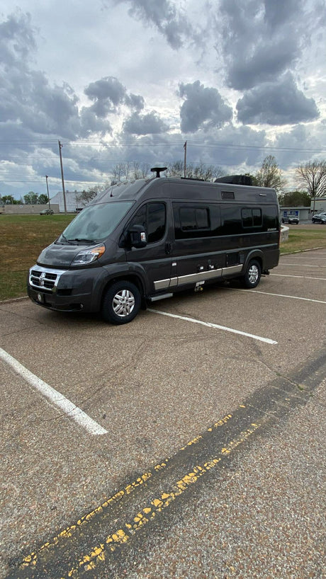 A dark grey ProMaster Class B RV, perfect for an rv rental adventure, parked in a lot under a cloudy sky.