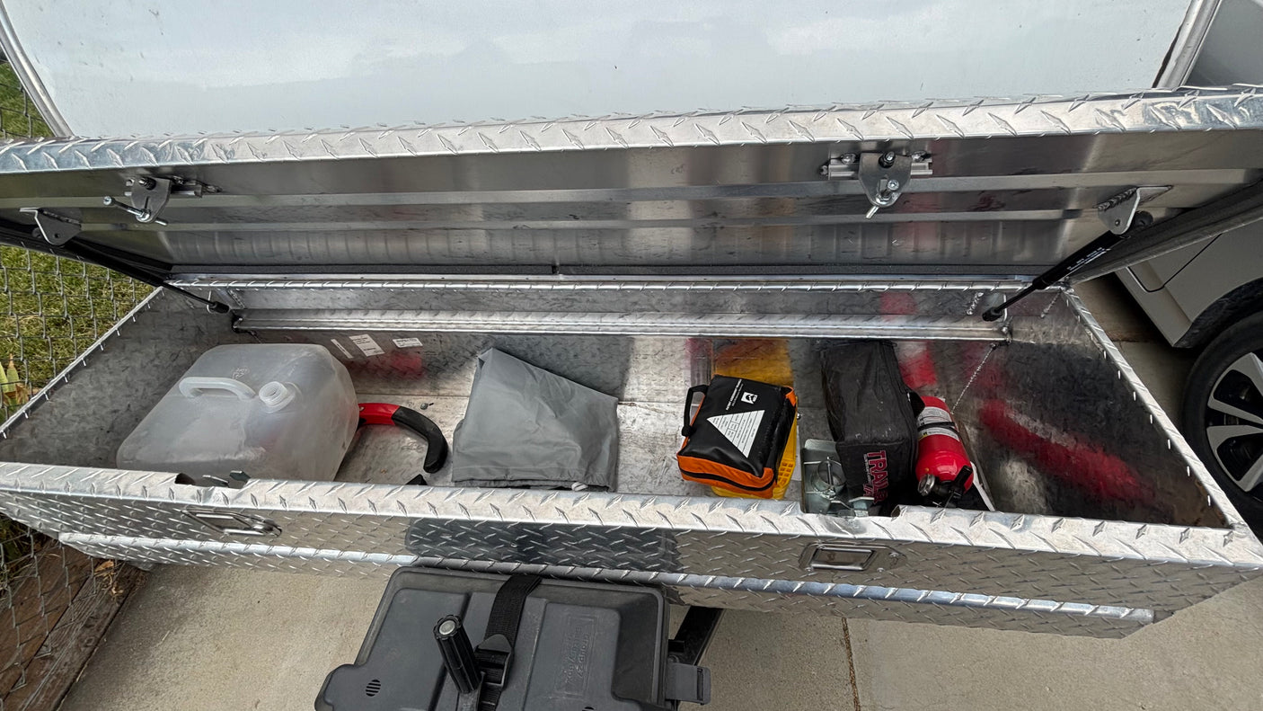 Inside an RV rental storage compartment, featuring essential safety gear: water jug, first aid kit, and fire extinguisher.