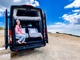 Woman in her RV rental van, featuring bunk beds, enjoys the ocean view from a scenic coastal overlook. Perfect for travel!