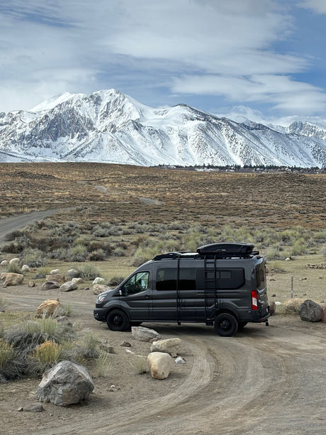 Explore nature with this **rv rental** van, parked in a scenic rocky landscape with majestic snow-capped mountains.