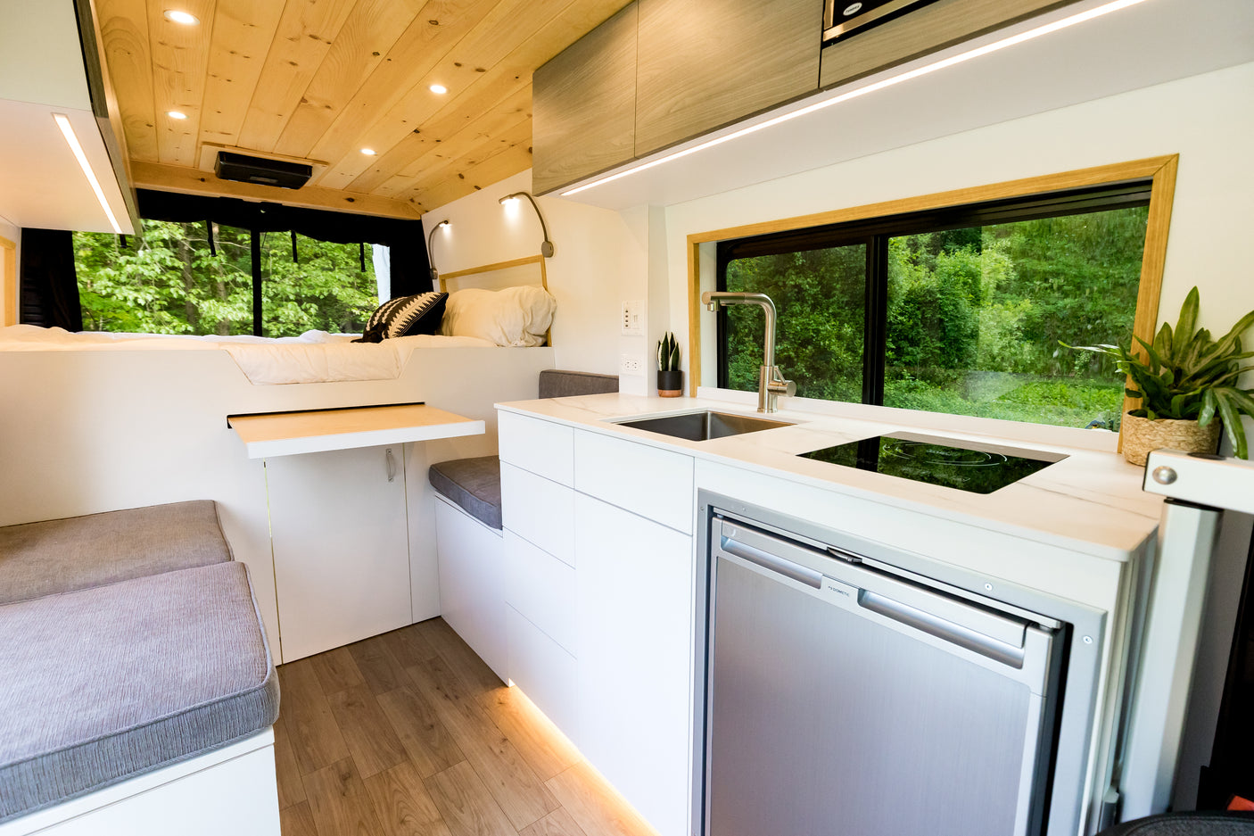 Explore in comfort! This bright **rv rental** features a modern kitchen, comfy bed, and dining nook with forest views.