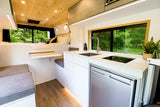 Explore in comfort! This bright **rv rental** features a modern kitchen, comfy bed, and dining nook with forest views.