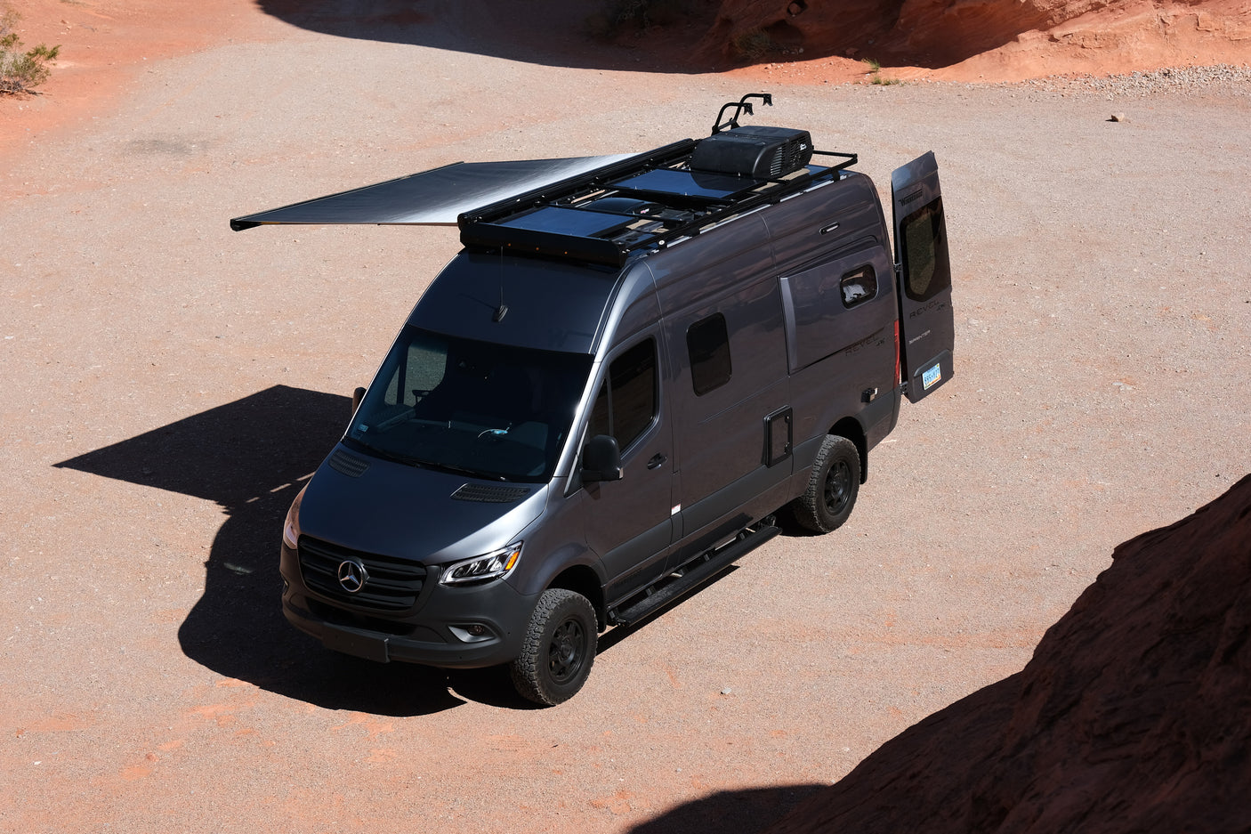 A gray Mercedes-Benz Sprinter Winnebago Revel 4x4 rv rental, with an extended awning, is ready for desert adventures.
