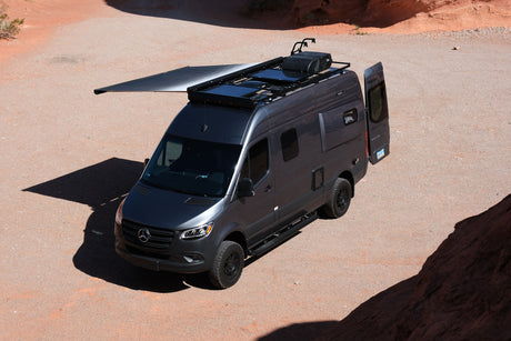 A gray Mercedes-Benz Sprinter Winnebago Revel 4x4 rv rental, with an extended awning, is ready for desert adventures.