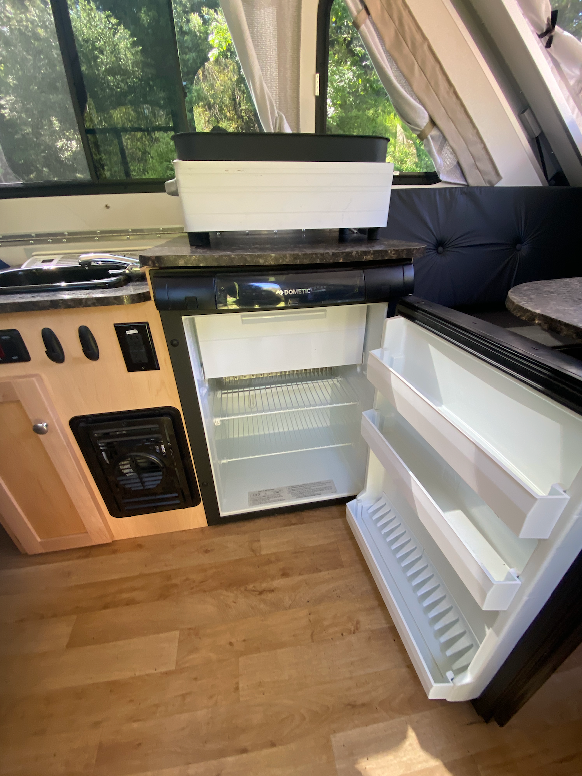 Compact RV rental kitchen with open Dometic fridge, sink, and griddle, perfect for road trip adventures.