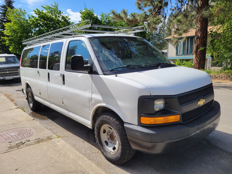 White cargo van with roof rack, a versatile choice for an rv rental conversion, parked on a sunny street.