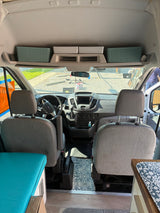 Inside this RV rental camper van, see the front seats, dashboard, and overhead storage bins from the living area.