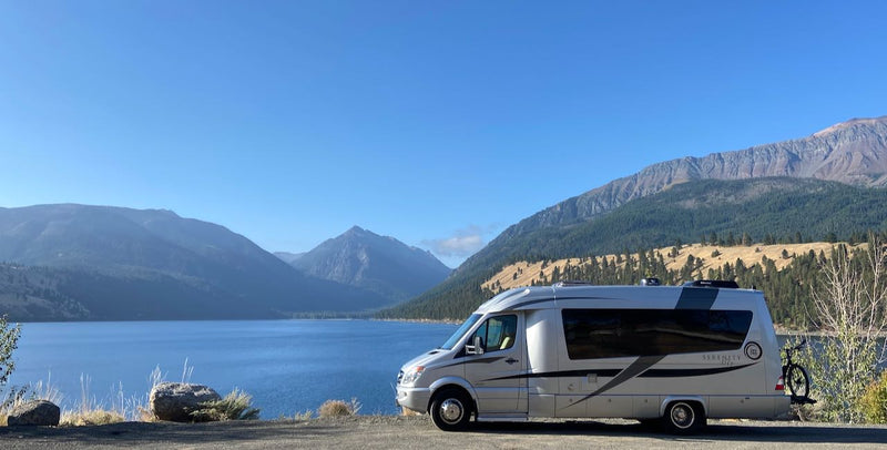  parked by the water with an old boat and cloudy sky. Perfect for coastal adventures.|Silver RV rental parked by a large blue lake with majestic mountains under a clear sky. A perfect scenic getaway.|Silver RV rental with bikes parked amidst unique desert rock formations. Perfect for a scenic road trip adventure.|RV rental interior: A cozy — photo 1