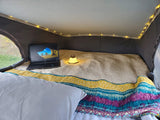Cozy RV rental bed setup: laptop, glowing lantern, and warm string lights create a perfect mobile workspace.
