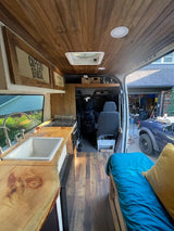 This RV rental van conversion features live-edge wood counters, kitchen, and comfy bed for mobile living.