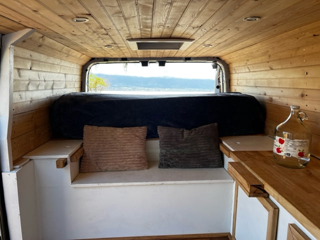 Cozy RV rental interior featuring wood paneling, a bed, and stunning lake views, ideal for your next van life adventure.