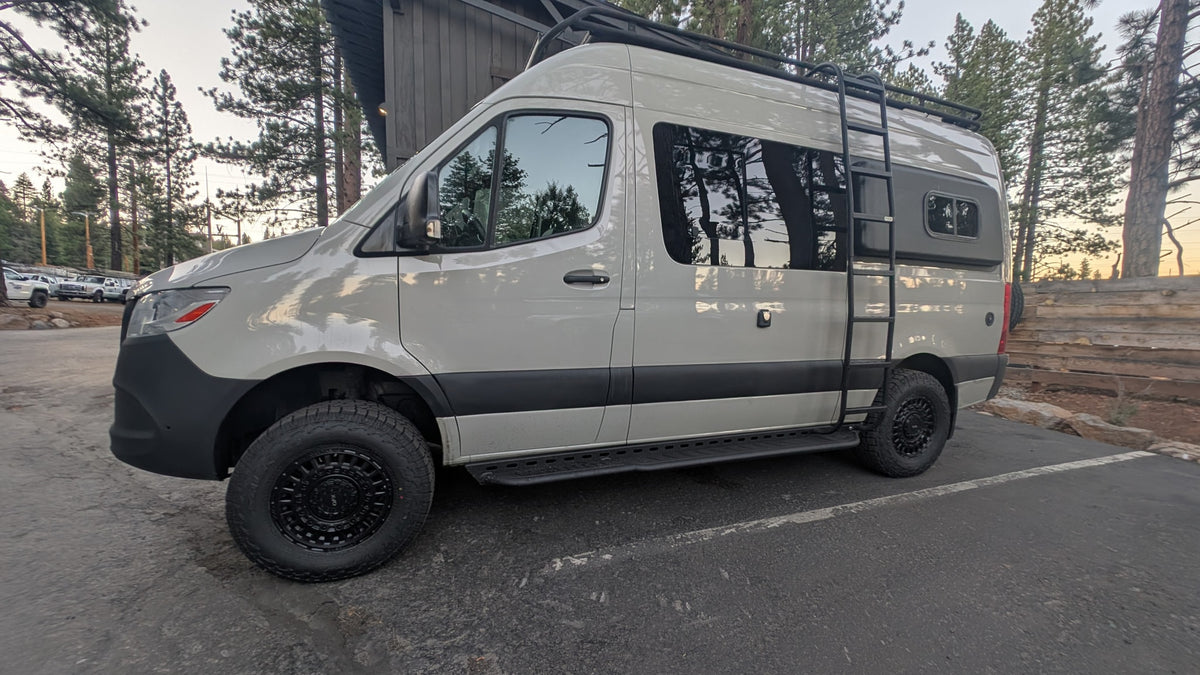 Adventure-ready white Mercedes Sprinter RV rental with off-road tires and roof rack, parked in a scenic forest setting. — photo 13