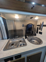 RV rental kitchenette showing a compact two-burner stove, sink with pull-down faucet, and magnetic knife rack.