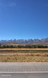 Scenic snow-capped mountains, golden fields, and clear blue sky from a moving vehicle. Perfect for an RV rental road trip.
