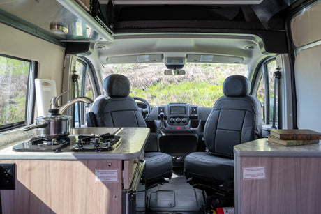 An RV rental interior with a kitchenette (stove, sink), swiveling front seats, and dashboard. Ideal for comfortable road trips.