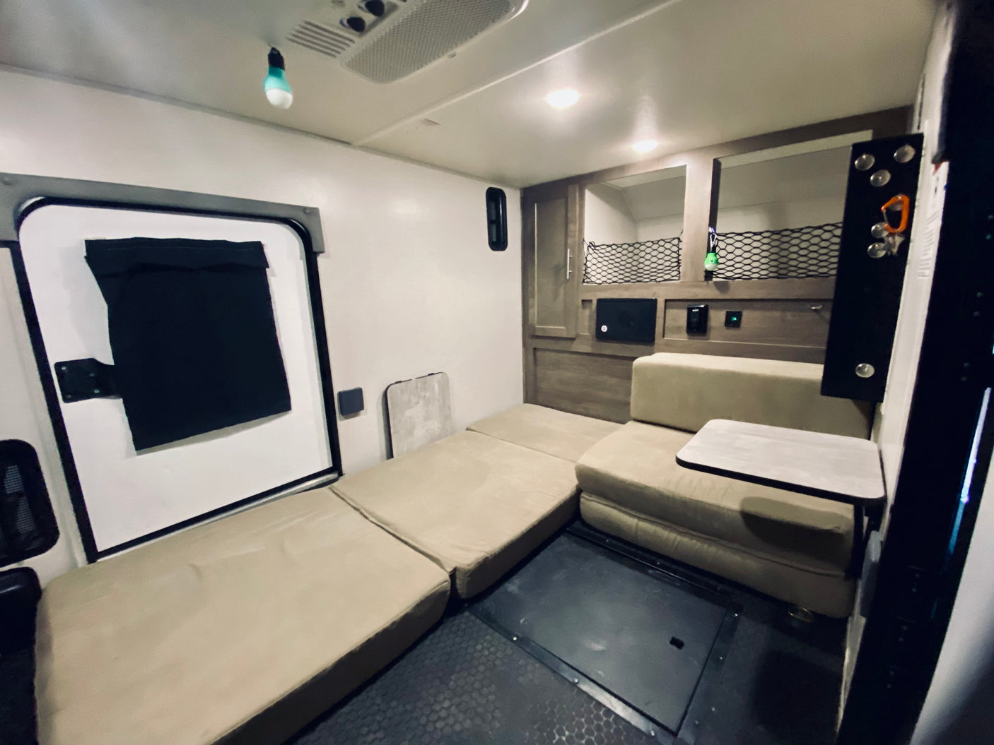 Spacious RV rental interior with versatile beige seating/bed, door, storage, and ceiling AC unit.
