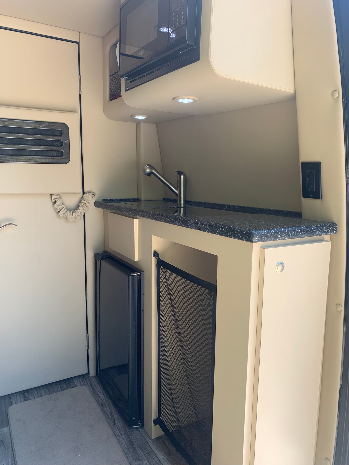 RV rental's compact kitchen interior shows a sink, microwave, fridge, and smart storage solutions for efficient travel.
