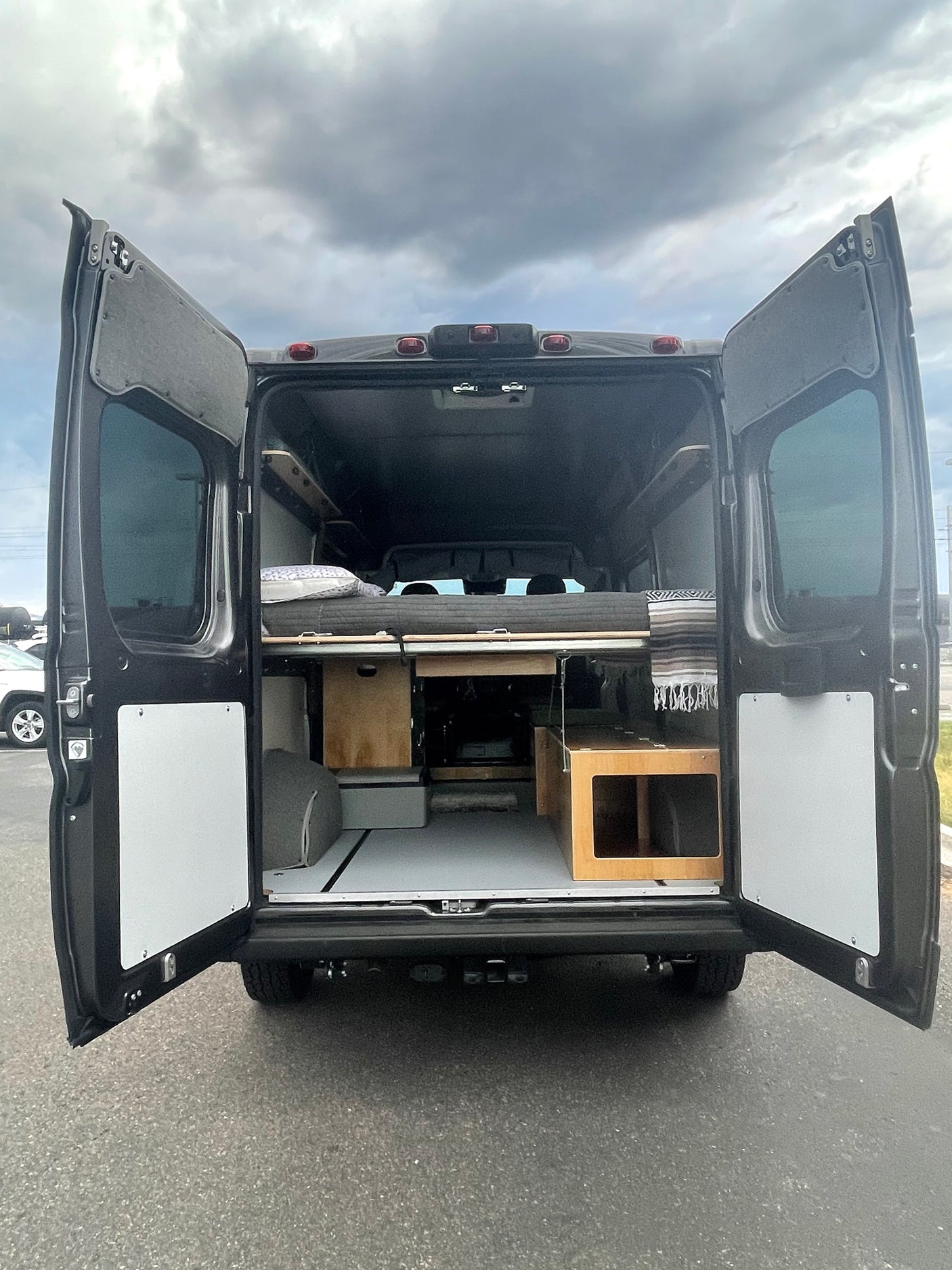 RV rental: Rear view of a dark camper van conversion, showcasing the comfortable bed and ample storage within.
