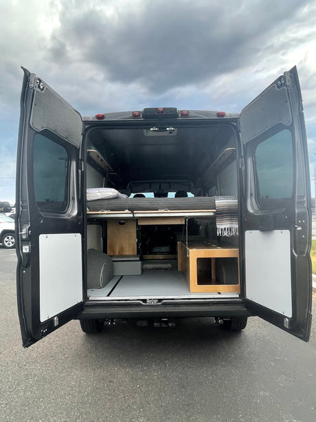 RV rental: Rear view of a dark camper van conversion, showcasing the comfortable bed and ample storage within.