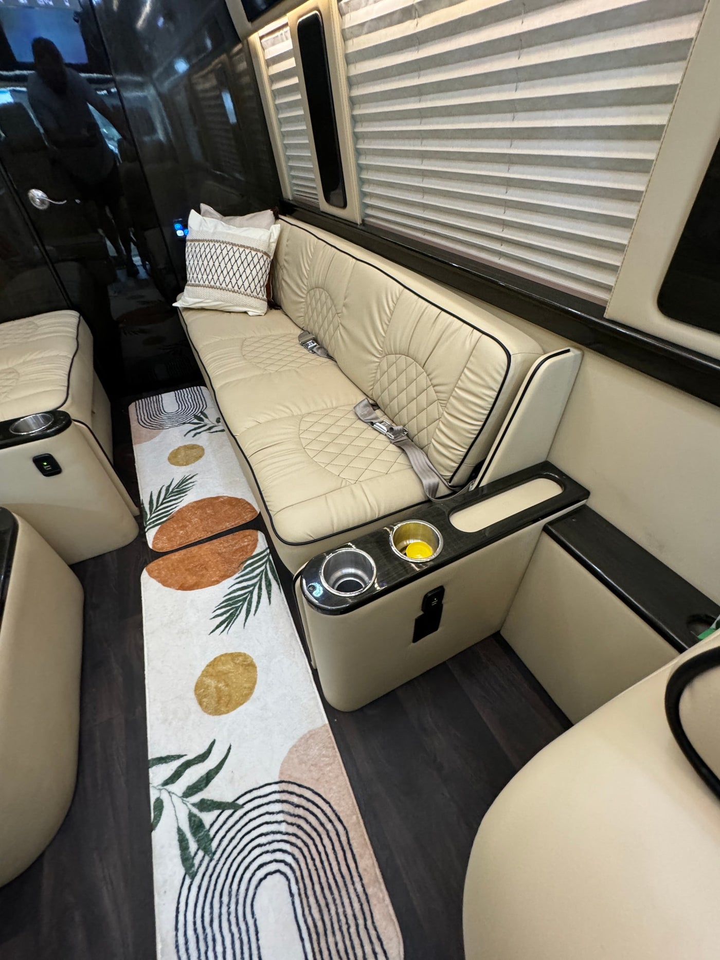 Luxury RV rental interior: comfortable beige bench seating with seatbelts, cup holders, charging port, and decorative rug. — photo 6