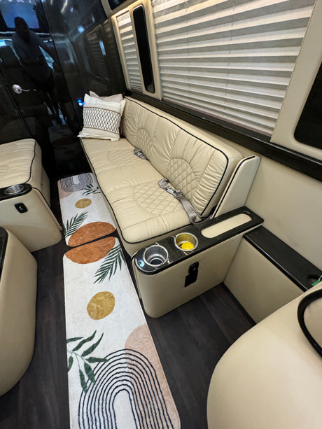 Luxury RV rental interior: comfortable beige bench seating with seatbelts, cup holders, charging port, and decorative rug.