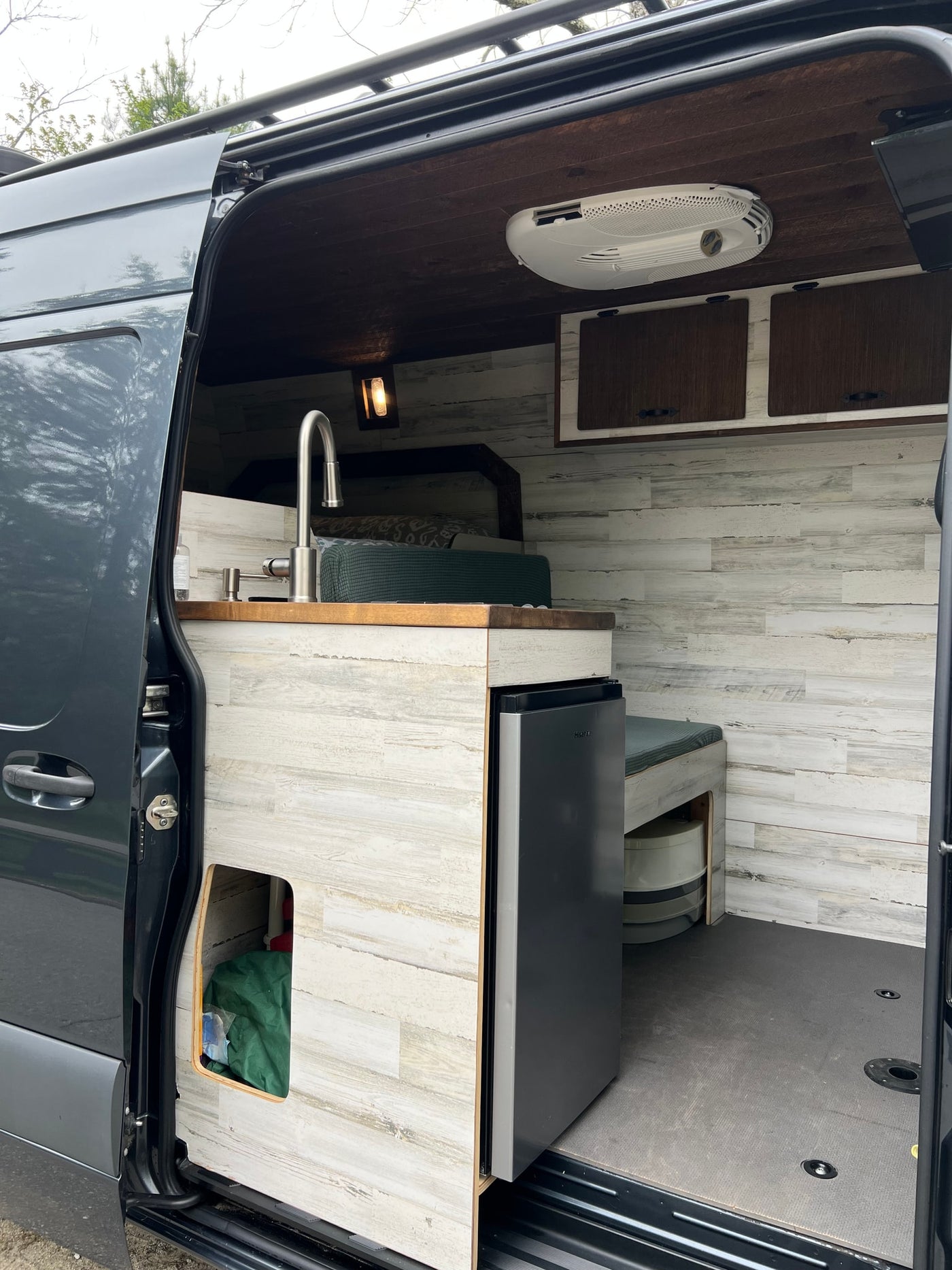 Modern RV rental interior: Custom camper van with sink, fridge, wooden accents, and a cozy bed visible through the open door. — photo 9