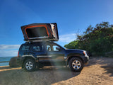 Black SUV with open rooftop tent on a sunny beach. Perfect RV rental for your next outdoor camping adventure.