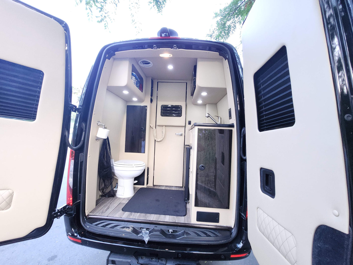 Rear view of an RV rental camper van's well-equipped interior with a toilet, sink, and bright lighting.