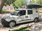 White Ram ProMaster City camper van, with roof box & custom graphic, ready for rv rental adventures. Driver smiles.