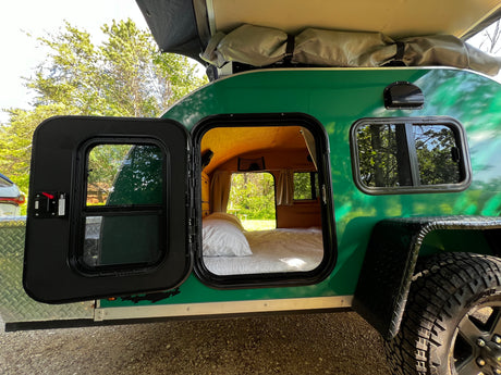 Green teardrop RV rental with open door revealing a cozy bed inside. Ideal for compact camping trips.
